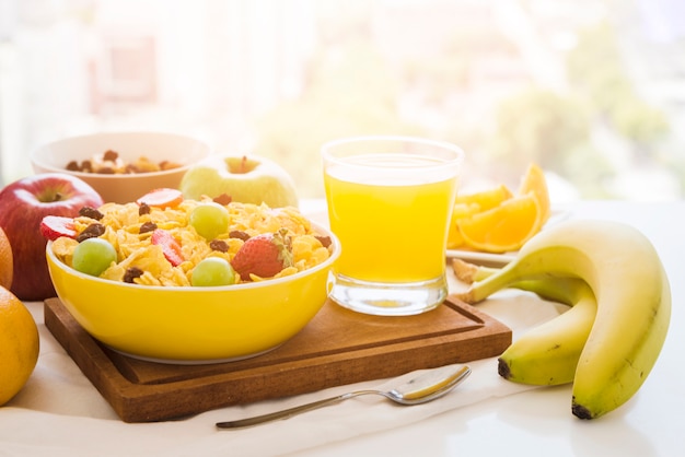 Foto cornflakes con frutta; bicchiere di succo sul tagliere sopra il tavolo