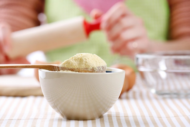 Photo cornmeal in bowl with wooden spoon on table close up