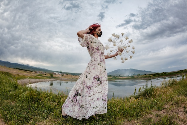 Корона мода. Драматический снимок девушки с красными волосами, держащей декоративный шар с короной и идущей рядом с озером