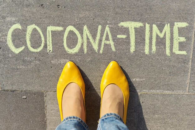 Corona time concept, top view on woman legs and text written in chalk on gray sidewalk.