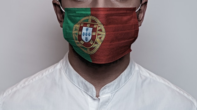 コロナウイルスパンデミック。コロナウイルス検疫の概念、Covid-19。男性の顔はポルトガルの旗の色で塗られた保護用医療マスクで覆われています