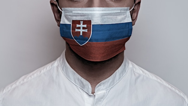 Corona virus pandemic. Concept of Corona virus quarantine, Covid-19. The male face is covered with a protective medical mask, painted in Slovakia flag colors