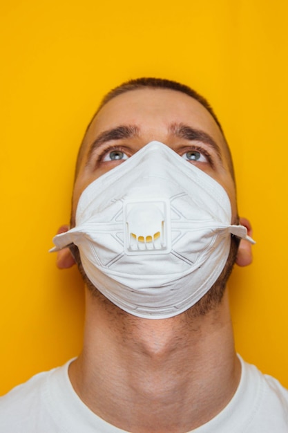 Corona virus Young guy in a respirator on a yellow background Protection of the mouth and eyes from viruses infections exhaust fumes Methods for the prevention of infection Vertical photo