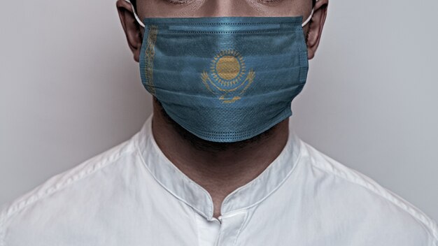Coronapandemie. Concept van quarantaine van het Corona-virus, Covid-19. Het mannelijke gezicht is bedekt met een beschermend medisch masker, geschilderd in de kleuren van de Kazachstaanse vlag