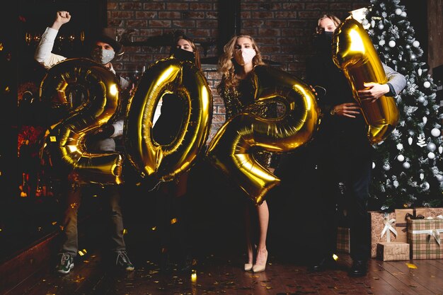 Coronapandemie. Feest, mensen en nieuwjaarsvakantieconcept - vrouwen en mannen met beschermend medisch masker vieren oudejaarsavond 2021