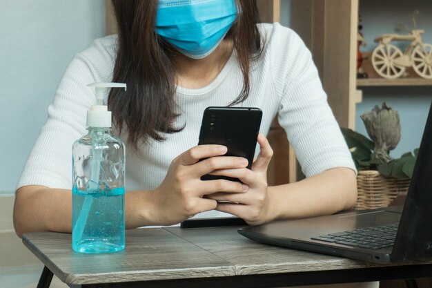 Coronavirus. Business woman working from home wearing protective mask. Working from home. Cleaning her hands with sanitizer gel.