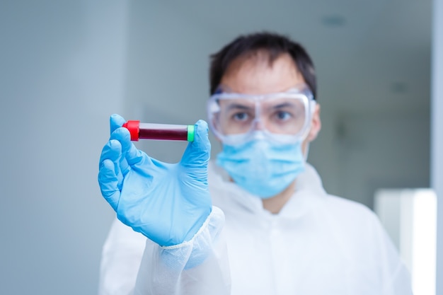 coronavirus covid 19 infected blood sample in sample tube in hand of scientist with biohazard protection clothing in coronavirus covid 19 reseach laboratory, coronavirus covid-19 vaccine research