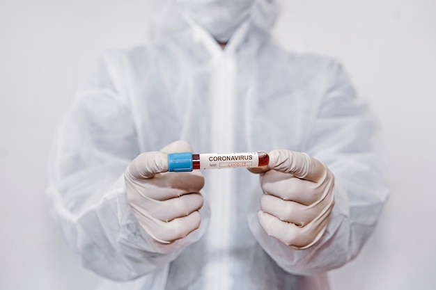 코로나바이러스 코비드 19 연구 실험실에서 생물학적 위험 보호복을 입은 과학자의 손에 있는 샘플 튜브에 있는 코로나바이러스 코비드 19 감염 혈액 샘플. 혈액으로 시험관을 들고 의사 손