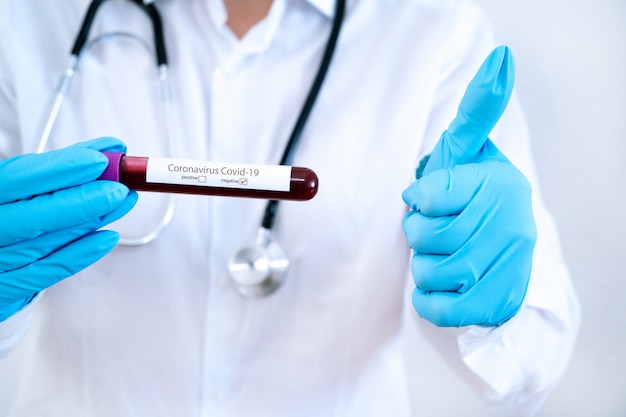 コロナウイルスCovid-19発生。医学と流行のコンセプト。血液検査結果が陽性のチューブ、防護マスク、薬、聴診器、バイアルとシリンジ、実験室のワクチン