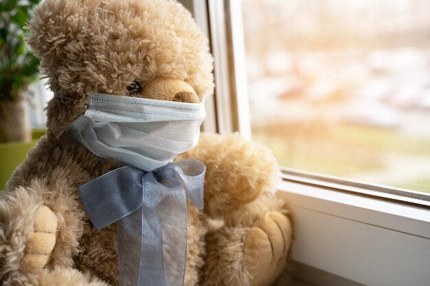 Coronavirus covid-19 and pollution protection concept. teddy bear doll wearing mask, sits on windowsill. Medical care, Quarantine 2020