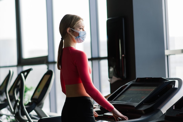 Coronavirus covid-19 preventie, fitness meisje met een medisch masker poseren in de sportschool. Virussen bestrijden.