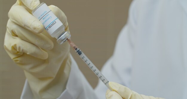 Вакцина против коронавируса COVID-19. Врач держит вакцину против вируса короны и использует шприц для предотвращения заражения COVID-19.