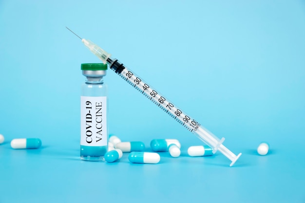 Coronavirus COVID-19 vaccine in glass bottle, pills and syringe on blue background.