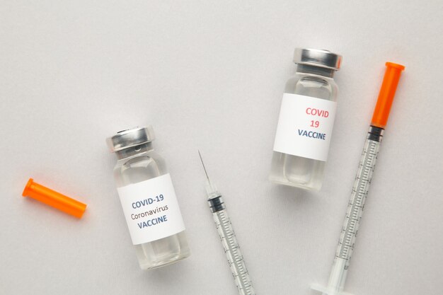 Coronavirus COVID-19-vaccinflesjes en spuit op grijs met kopie ruimteachtergrond. Bovenaanzicht