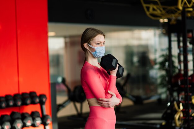 Coronavirus covid prevention, fitness girl with medical mask holding a dumbbell . Fighting viruses.