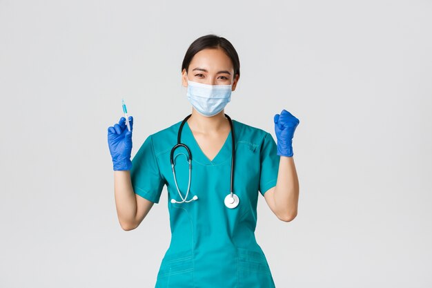 , 코로나 바이러스 질병, 의료 종사자 개념. 명랑 승리 아시아 여성 의사, 의료 마스크와 장갑 의사, 백신 주사기를 들고 기뻐