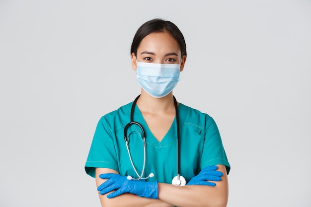 , coronavirus disease, healthcare workers concept. Close-up of confident smiling, professional asian doctor, nurse in medical mask and rubber gloves ready for examination, white wall