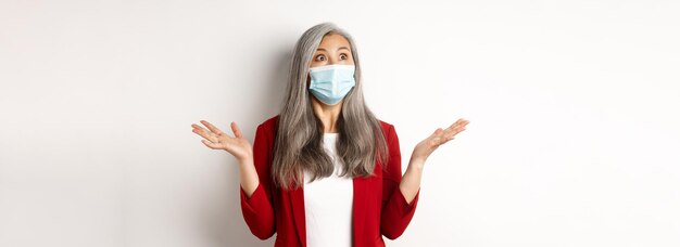 Coronavirus en bedrijfsconcept verraste Aziatische zakenvrouw met gezichtsmasker verspreidde handen zijwaarts