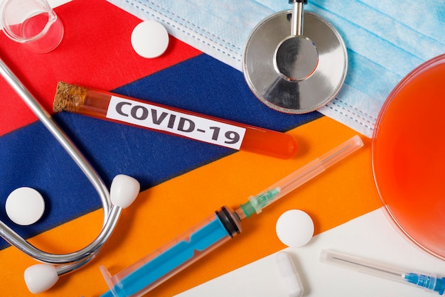 Coronavirus het concept COVid19 Bovenaanzicht beschermend ademhalingsmasker stethoscoop spuittabletten op de vlag van Armenië