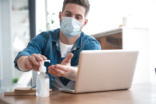 Coronavirus. Man aan het werk vanuit huis met een beschermend masker. Zijn handen reinigen met ontsmettingsgel.