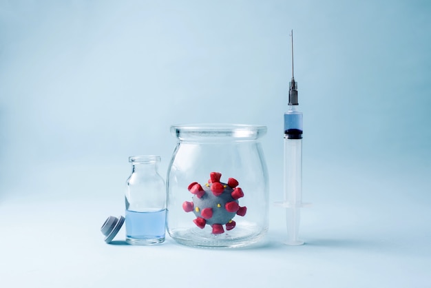 Coronavirus model in a glass jar, a syringe with a vaccine, a vaccine bottle, COVID-19 vaccine concept, close up.