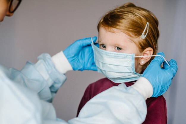 코로나 바이러스. 간호사, 보호 복에 의사, 아이의 얼굴에 의료 마스크를 착용. Covid-19 감염에 대한 예방 조치. 인플루엔자, 코로나 바이러스 전염병에 대한 보호의 개념.