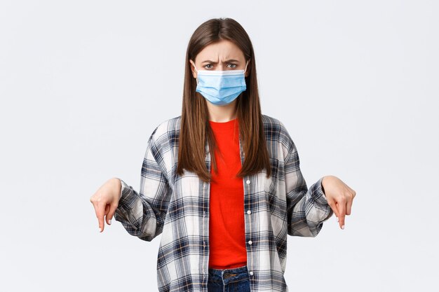 Coronavirus outbreak, leisure on quarantine, social distancing and emotions concept. Disappointed and angry young woman disapprove smth, pointing fingers down and frowning judgemental.