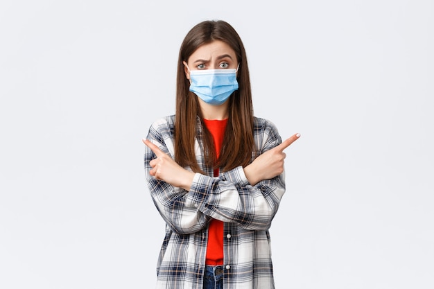 Coronavirus outbreak, leisure on quarantine, social distancing and emotions concept. Indecisive and clueless pretty girl in medical mask ask your opinion, advice as pointing sideways left and right.
