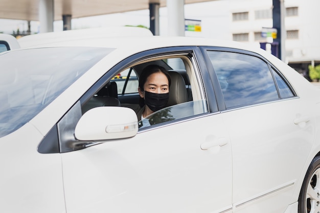 防護マスクを持つコロナウイルスパンデミックコンセプト女性が車の遠征旅行に座っています。