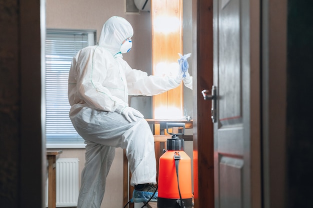 Coronavirus Pandemic A disinfector in a protective suit and mask sprays disinfectants in house