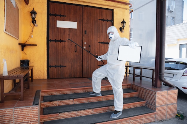 Coronavirus Pandemic A disinfector in a protective suit and mask sprays disinfectants in house