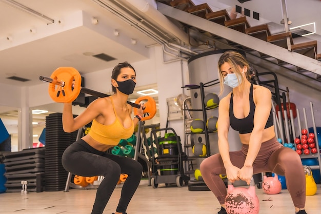 Coronavirus pandemic in gyms Two girls training with weights with face masks