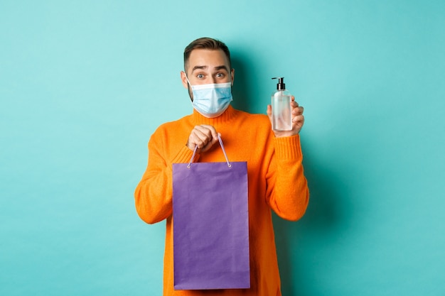 Coronavirus, pandemic and lifestyle concept. Man in face mask showing shopping bag and hand