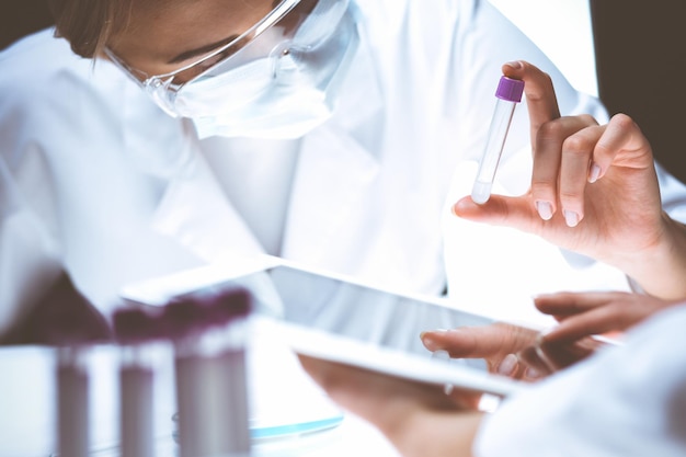 Photo coronavirus pandemic. professional female scientist in protective eyeglasses researching tube with reagents in laboratory. concepts of medicine and virus protection.