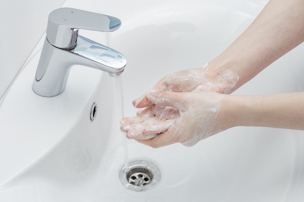コロナウイルス予防は、浴室のシンクの女性の手指衛生で抗菌石鹸で手を洗います。