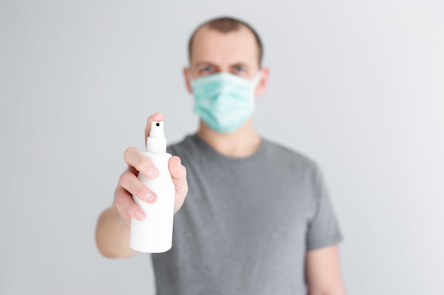 Coronavirus protection and disinfection concept - man in medical mask spraying sanitizer spray over white background