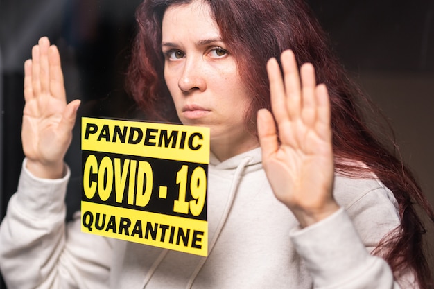 Foto coronavirus, quarantaine, covid-19 en pandemisch concept. verdrietige en zieke vrouw van het coronavirus kijkt door het raam