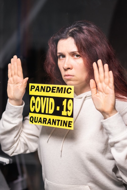 Coronavirus, quarantaine, covid-19 en pandemisch concept. Verdrietige en zieke vrouw van het coronavirus kijkt door het raam