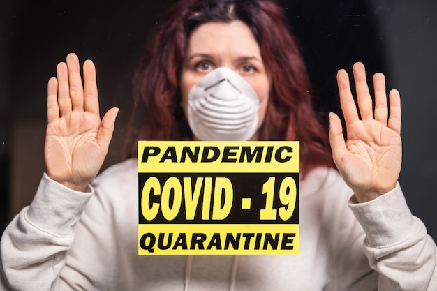 Foto coronavirus, quarantaine, covid-19 en pandemisch concept. verdrietige en zieke vrouw van het coronavirus kijkt door het raam