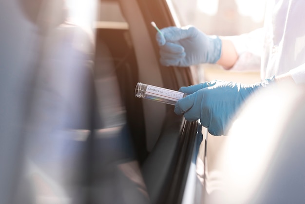 Coronavirus-test en persoon die handschoenen naast een auto draagt