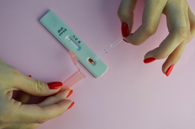 Тест на коронавирус на розовом матовом фоне. Девушка с ярко-красными ногтями делает медицинские процедуры