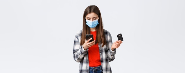 Coronavirus-uitbraak thuiswerken online winkelen en contactloos betalingsconcept Meisje met medisch masker met creditcardbestellingskleding met behulp van mobiele telefoontoepassing