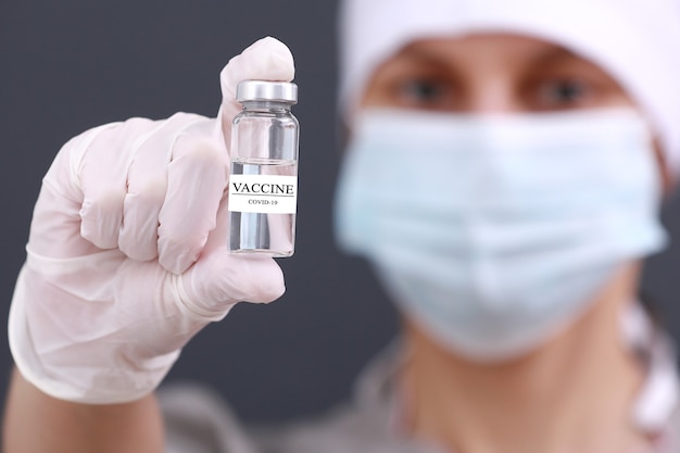 Coronavirus Vaccine COVID-19 in glass bottle in hand of female doctor in medical mask and gloves. Vaccine Concept