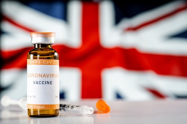 Вакцина от коронавируса COVID19 и медицинский шприц на фоне флага Соединенного Королевства