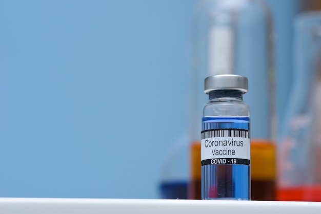 Фото Вакцина против коронавируса в бутылке для инъекций на столе на фоне медицинской лаборатории, место для текста. победить эпидемию коронавируса sars-cov-2.