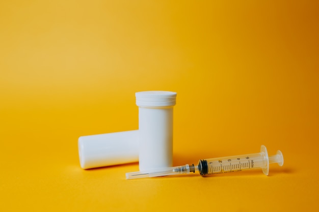 Coronavirus vaccine in white medicine jar on orange background. Pills for covid-19 curing.  Two white cans with pills and syringe on orange background.