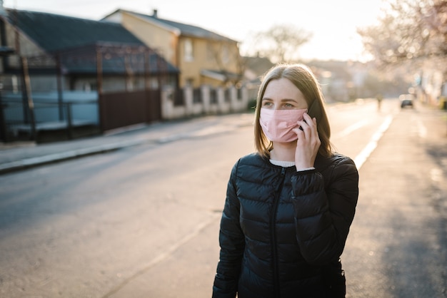 Coronavirus. Woman wearing medical protective mask talking on cell mobile phone, walking on street