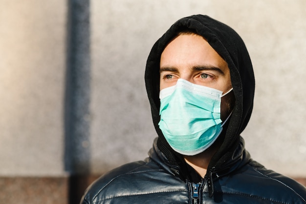 Coronavirus. Young man in city street wearing face mask protective for spreading of disease Covid-19. Close up of man with surgical mask on face against SARS-CoV-2. Pandemic.