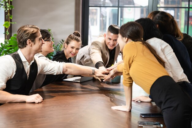 Il gruppo aziendale dei dipendenti che forma una pila di mani sul desktop con il leader manager per il successo del progetto