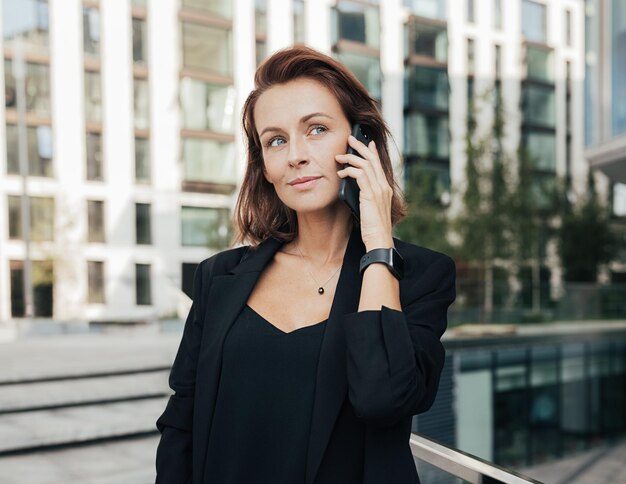 Photo corporate person with ginger hair standing outdoors and having a conversation by smartphone